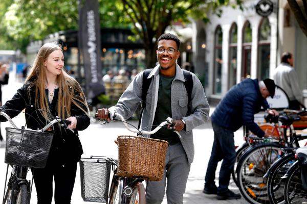 Två studenter leder cyklar pratar och ler i Karlstad centrum