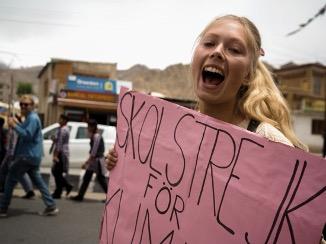Ung blond tjej som håller i ett plakat och ser glad ut