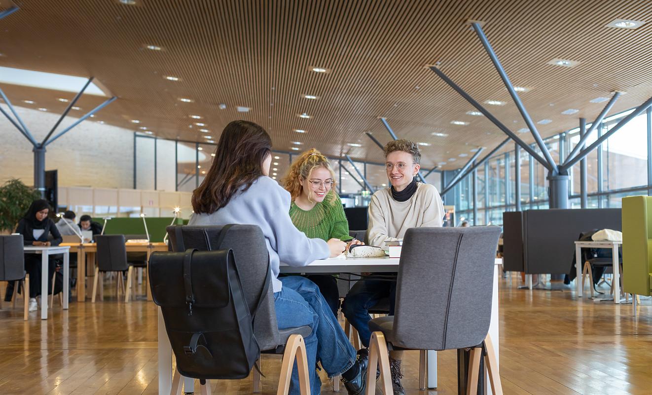 Tre studenter runt ett bord i biblioteket