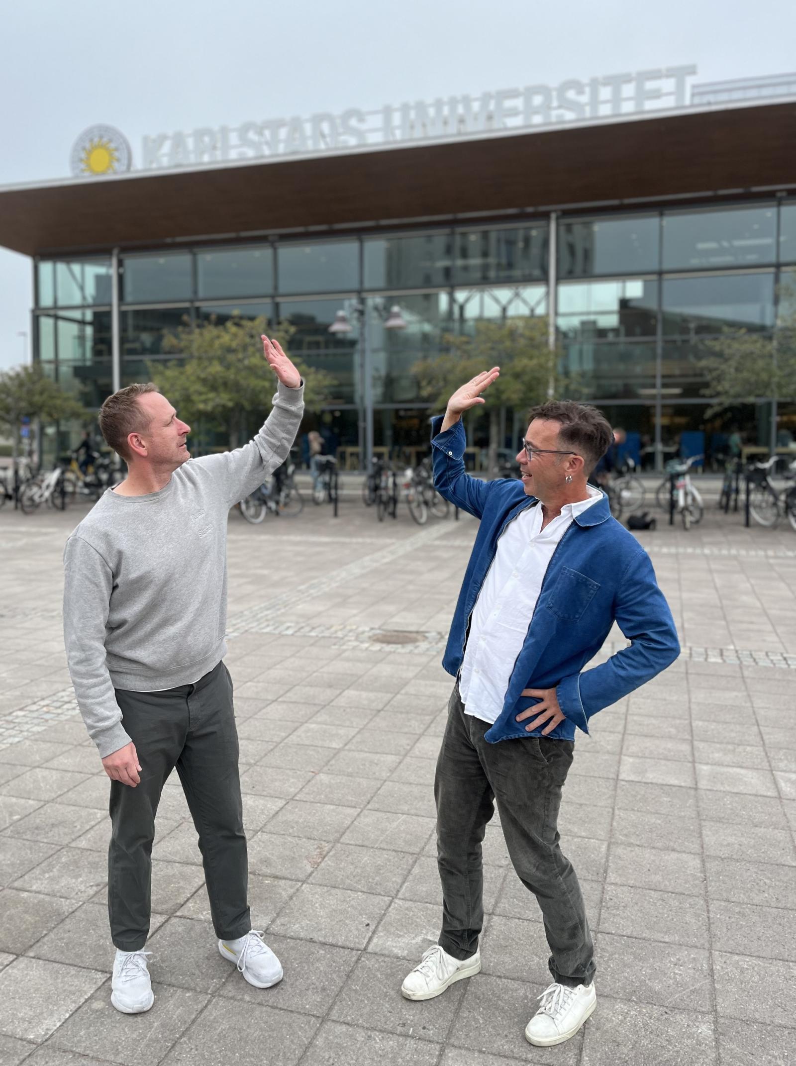 Två glada män gör high five framför universitetsbyggnaden