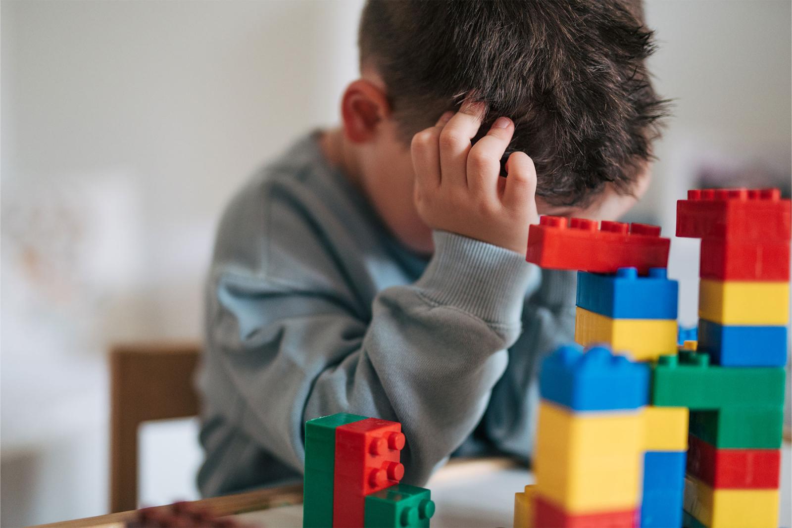Ung pojke med ansiktet i händerna framför lego
