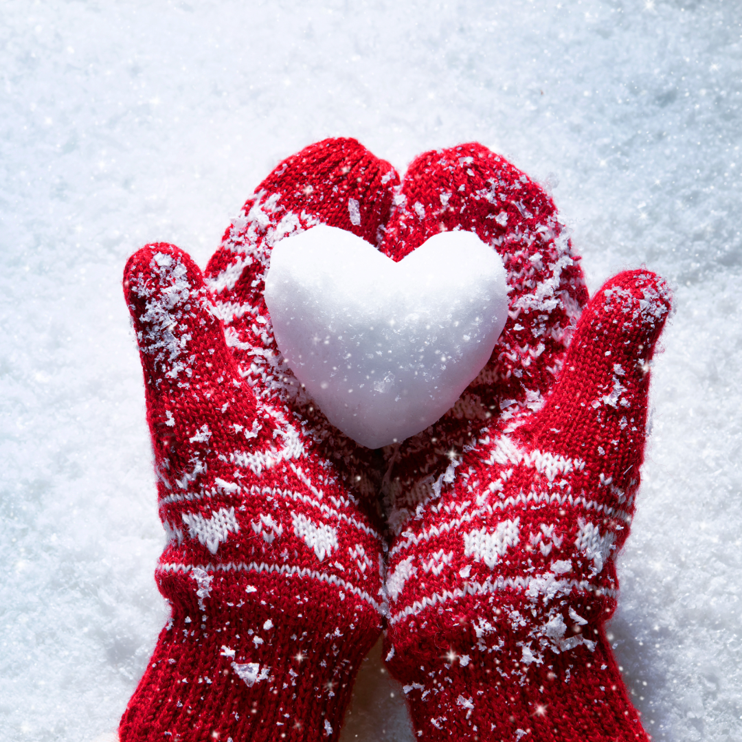 Händer med röda vantar som håller ett hjärta av snö