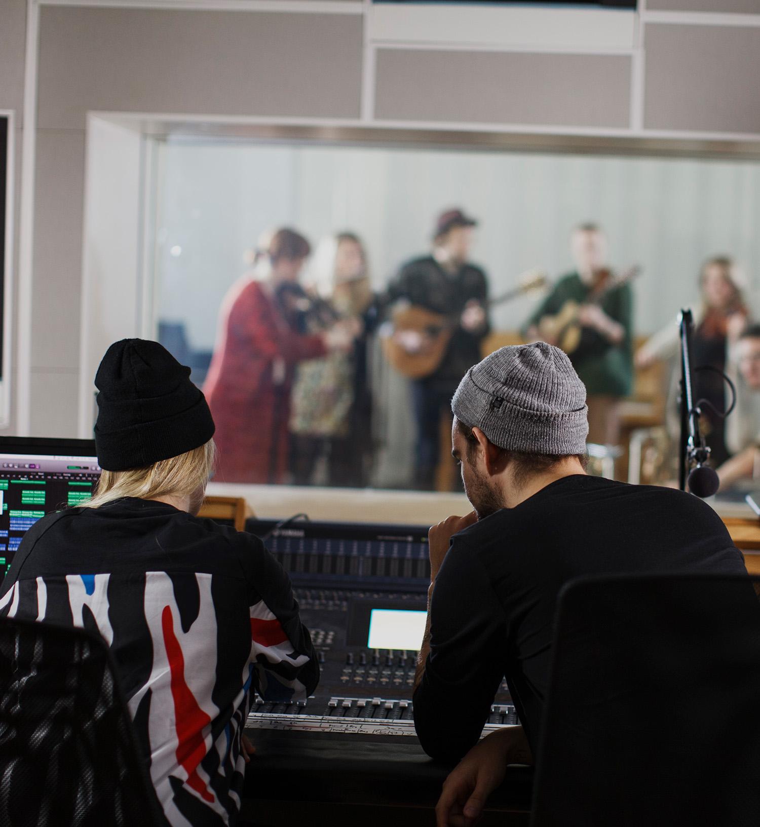 Två killar i en musikstudio framför ett mixerbord