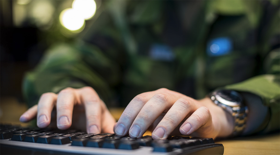 Händer som skriver på ett tangentbord med kamouflagekläder