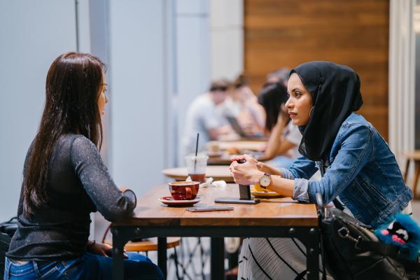 Två studenter sitter mitt emot varandra och dricker kaffe