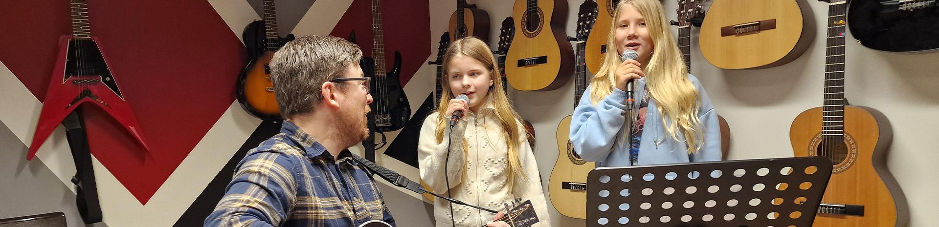musiklärare som spelar gitarr och två barn som sjunger