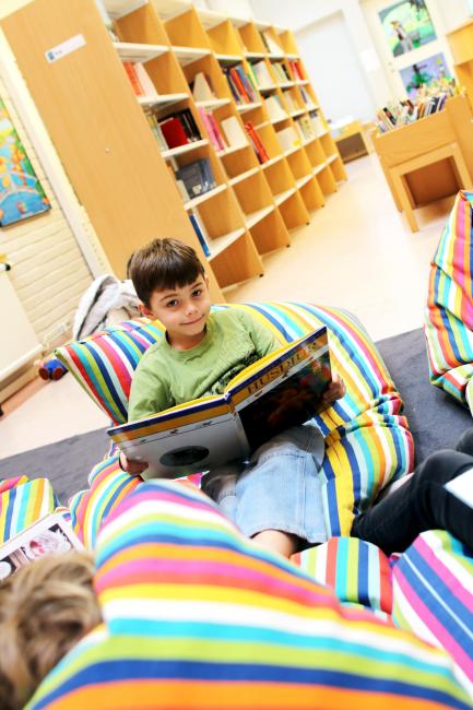 Liten pojke läser bok i bibliotek