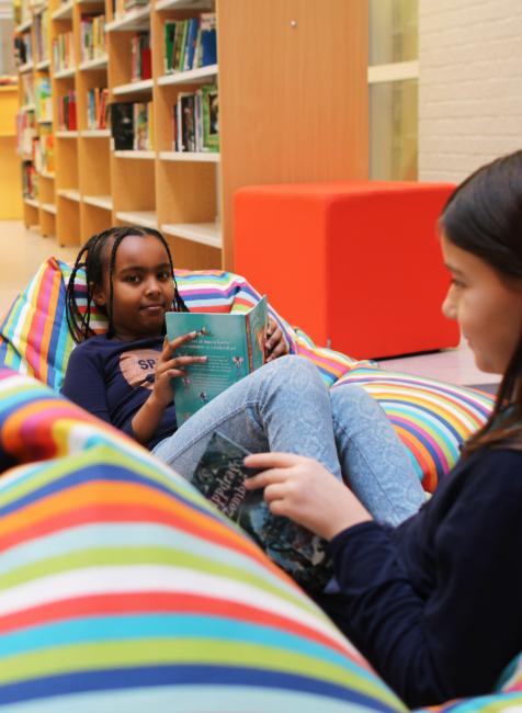 Liten flicka läser bok i bibliotek