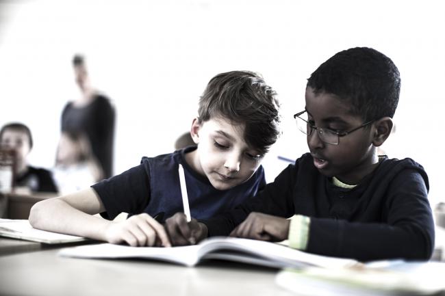 Två unga pojkar i klassrum skriver och läser tillsammans