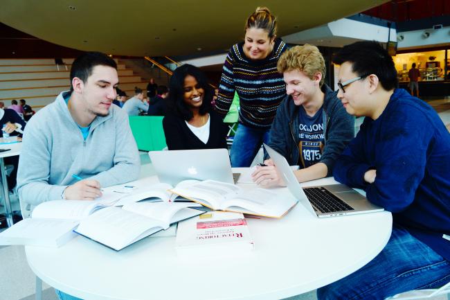 Fem studenter som läser och diskuterar runt ett bord på Karlstads universitet. 