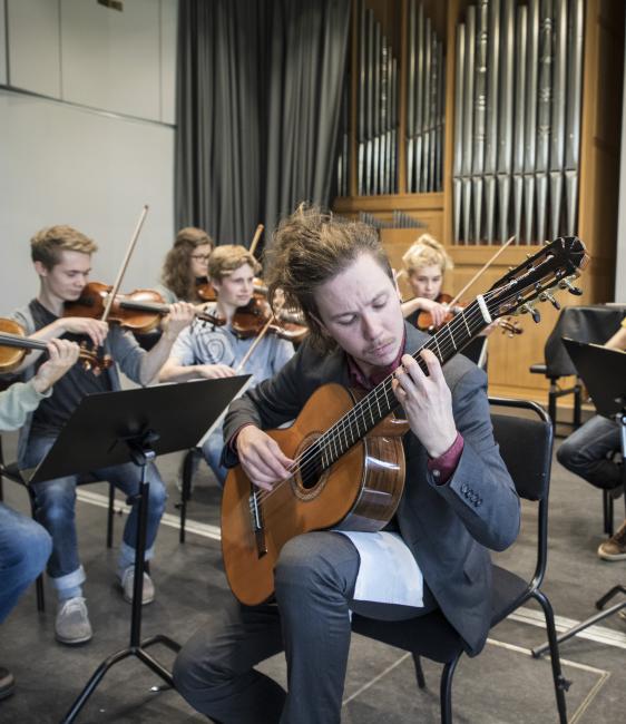 Gitarrist som spelar med violonister i bakgrunden