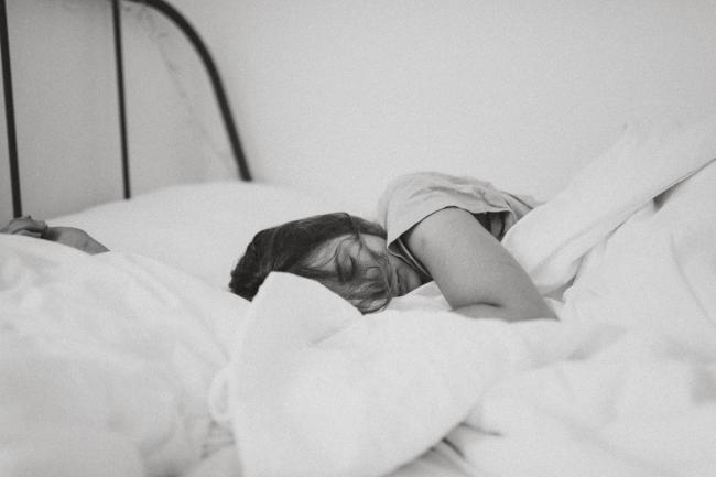 kvinna sover i säng med täcket uppdraget över sig