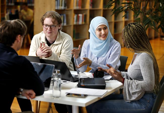 Tre studenter studerar och pratar tillsammans i biblioteket