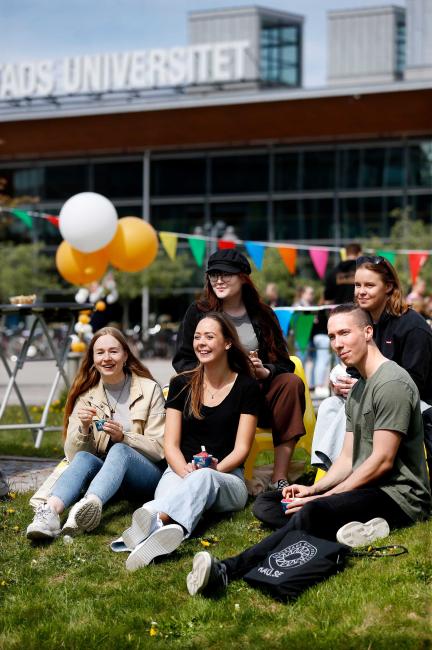 Fem studenter äter glass och har kul i gräset utanför huvudingången på campus
