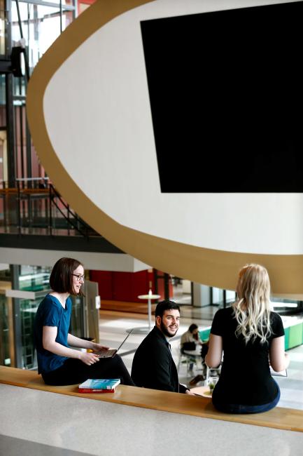 Tre studenter sitter i gradängen med Ljungbergsstudion i bakgrunden