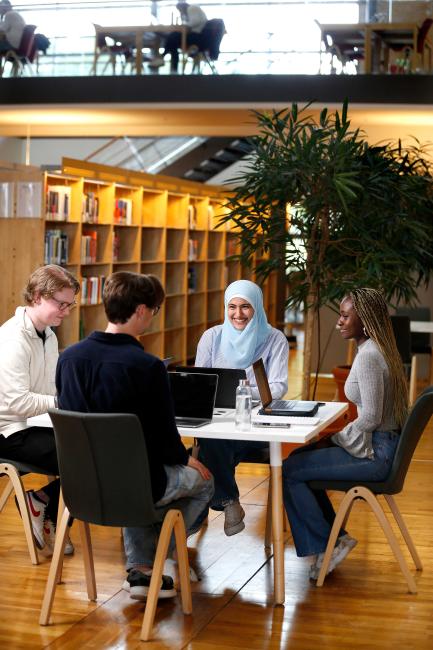 Fyra studenter sitter runt ett bord i biblioteket och pluggar