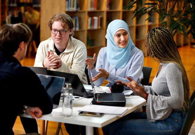 Fyra studenter sitter runt ett bord i biblioteket och diskuterar