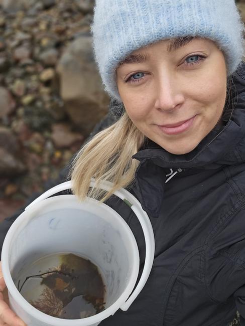 en ung tjej i mössa som håller i en plastburk med insekter och blad