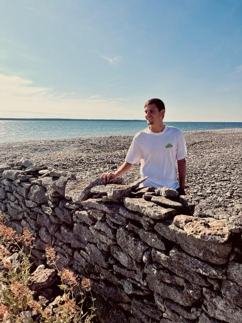 Jonathan står vid en stenmur med havet i bakgrunden