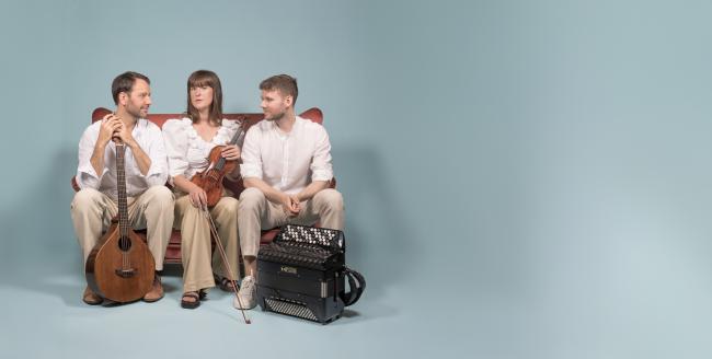 Musiktrio sitter på en bänk med sina instrument, violin, accordion, cittern