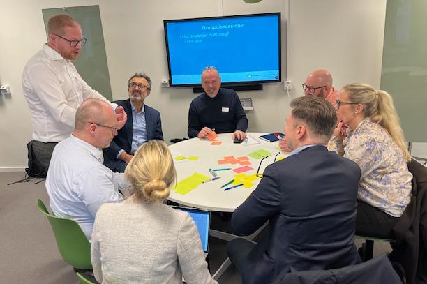 workshop  en stående man förklarar koncept för grupp sittande runt ett bord