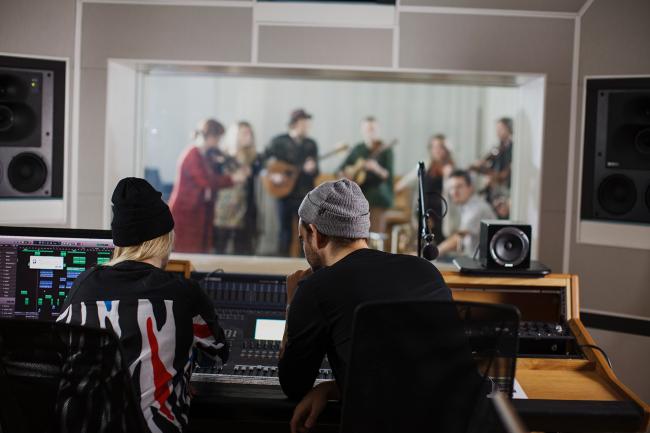 Två studenter sitter i en musikstudion framför ett mixerbord