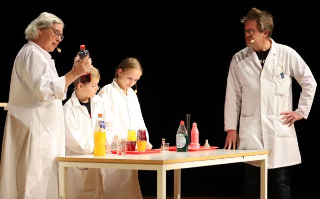 Två vuxna och två barn i labbrockar gör kemiexperiment vid ett bord