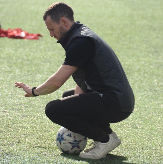 Man sitter på huk över en fotboll_James Vaughan_affilierad forskare vid Nationellt forskningscentrum för barn- och ungdomsidrott_2