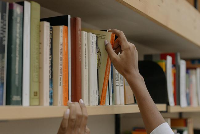 Bokhylla på bibliotek med händer som tar ut en bok