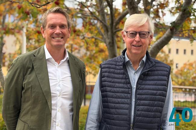 Två män står utomhus med höstlöv i bakgrunden